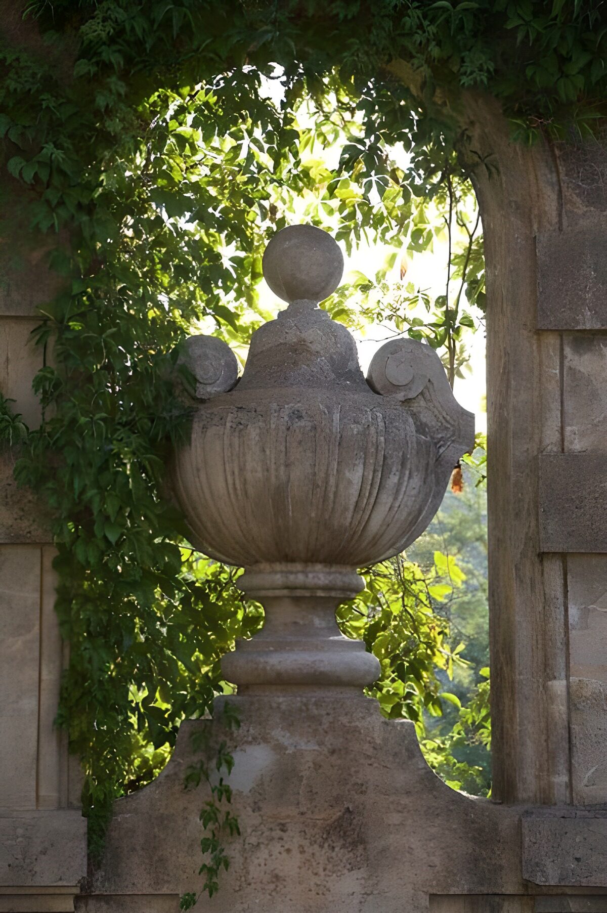 Urne en pierre sous une arche sertie de plantes grimpantes