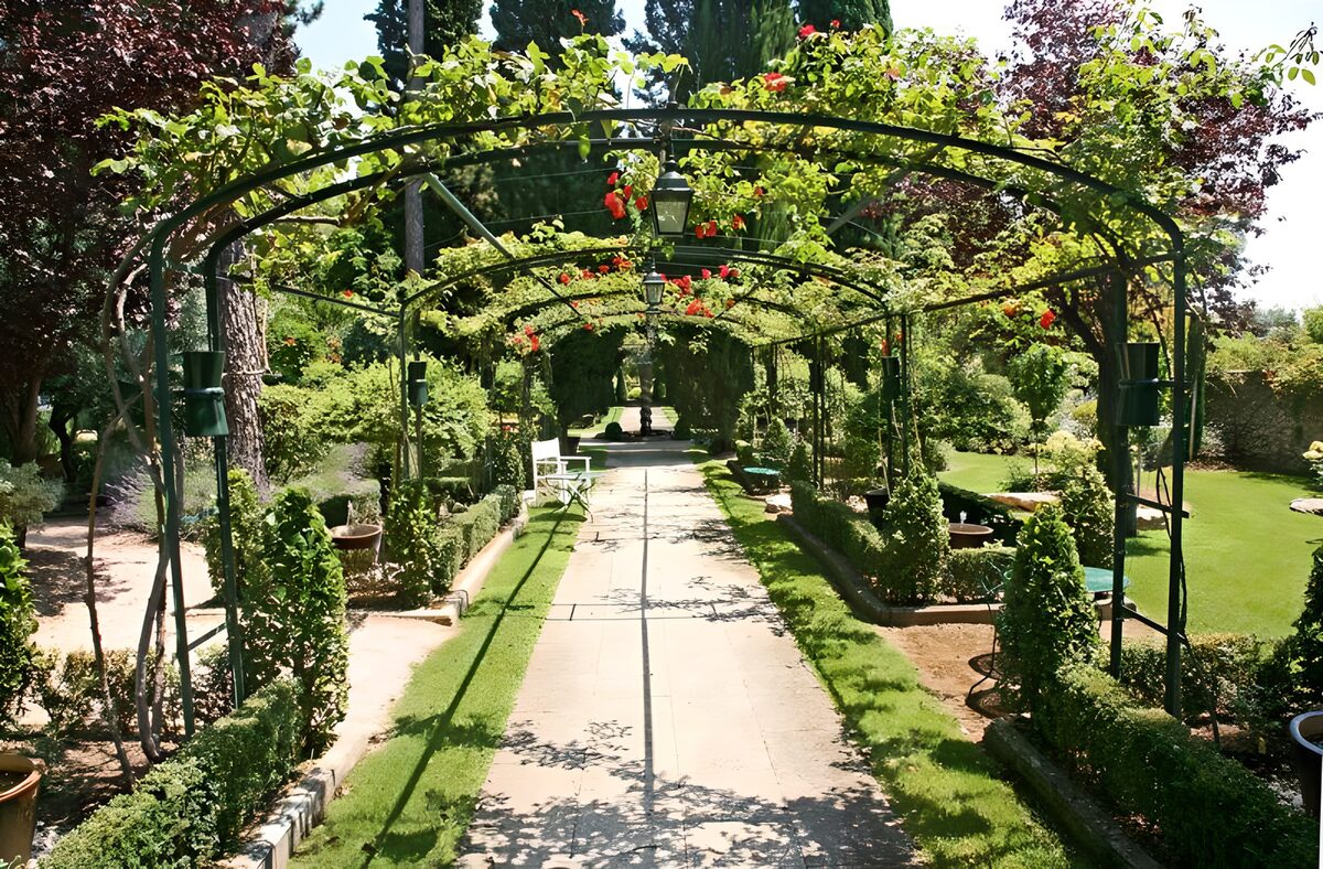 Vue sur un jardin à la française à travers des arches garnies de roses version 3